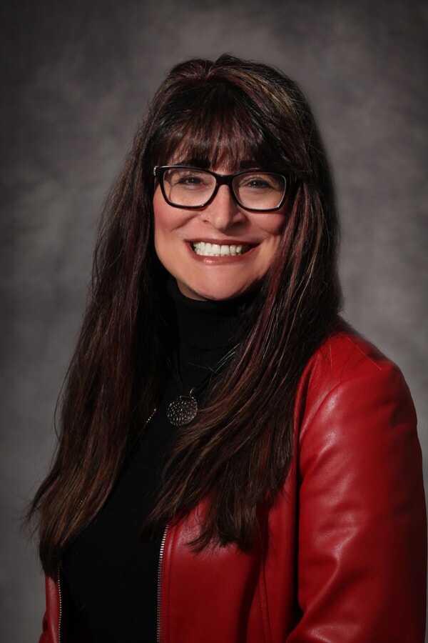 Irene Richardson, woman with long voluminous brown hair and black glasses wearing a red leather jacket